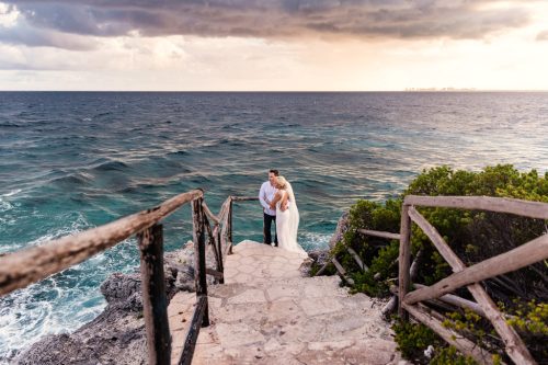 Bride and groom embrace on steps near ocean at their Isla Mujeres destination wedding