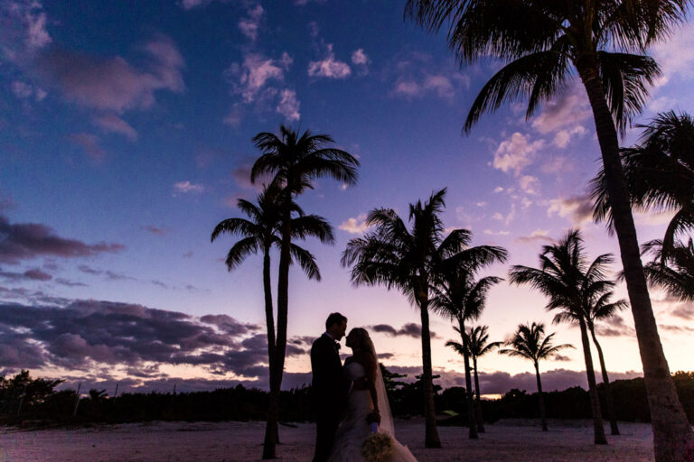 Romantic silhouette photo of bride and groom with palm trees and sunset at their Cancun, Mexico destination wedding