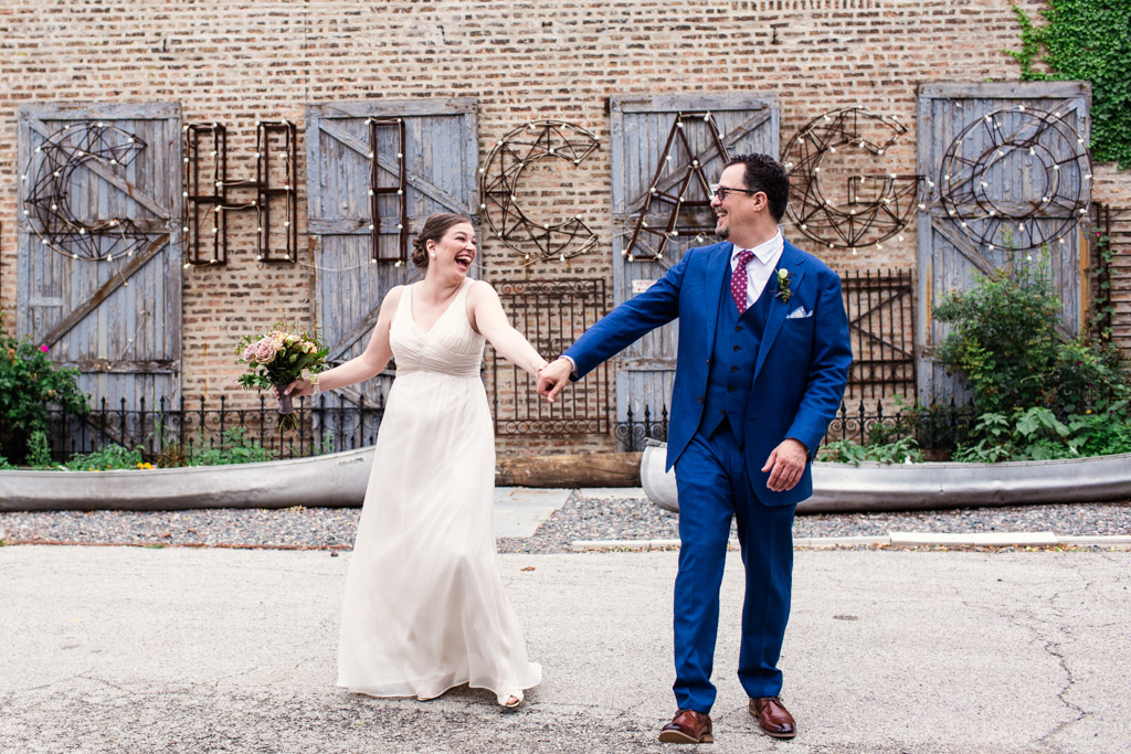 Bride and groom hold hands while smiling and walking through courtyard at Salvage One Chicago