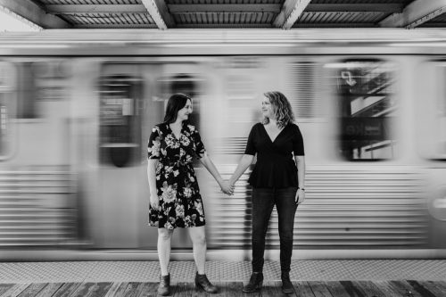 Bride and bride to-be hold hands at Clark & Lake stop for Chicago CTA engagement photo