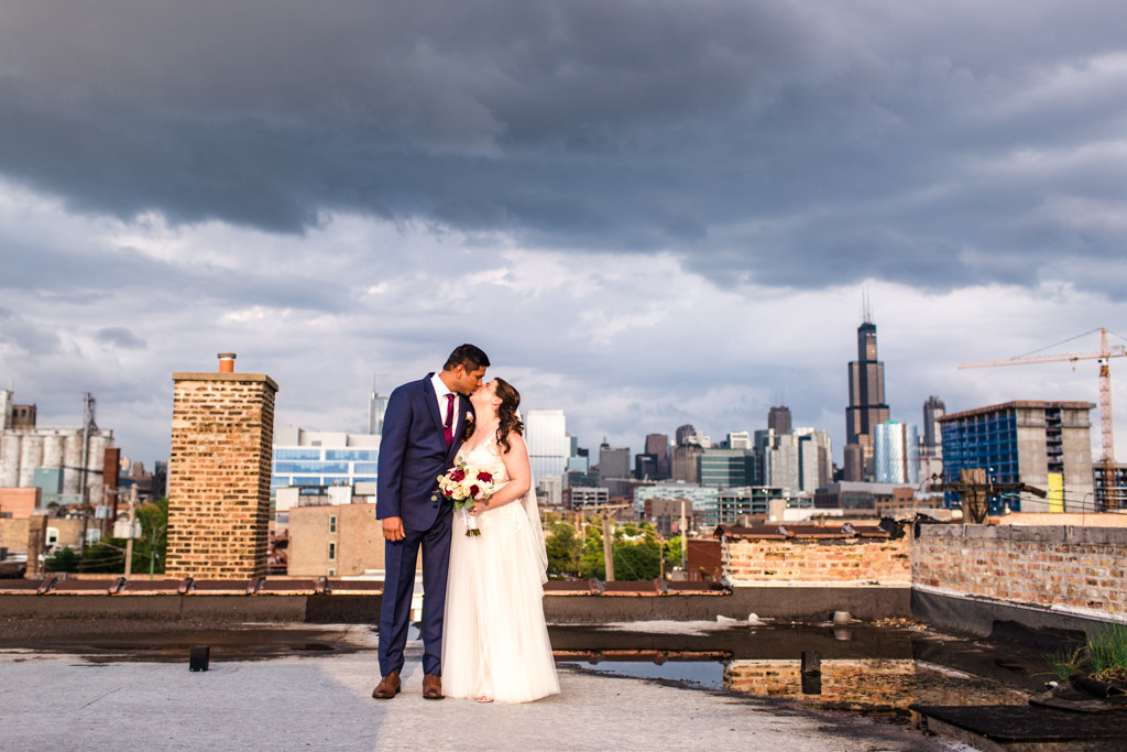 Bride and groom kiss on rooftop of their Room 1520 wedding with Chicago skyline and dramatic clouds