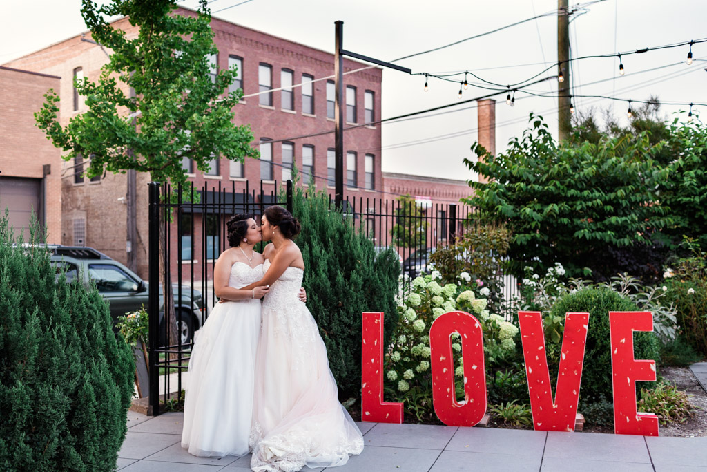 Chicago brides kiss in courtyard of their Concord Fifty Five wedding with LOVE letter decor