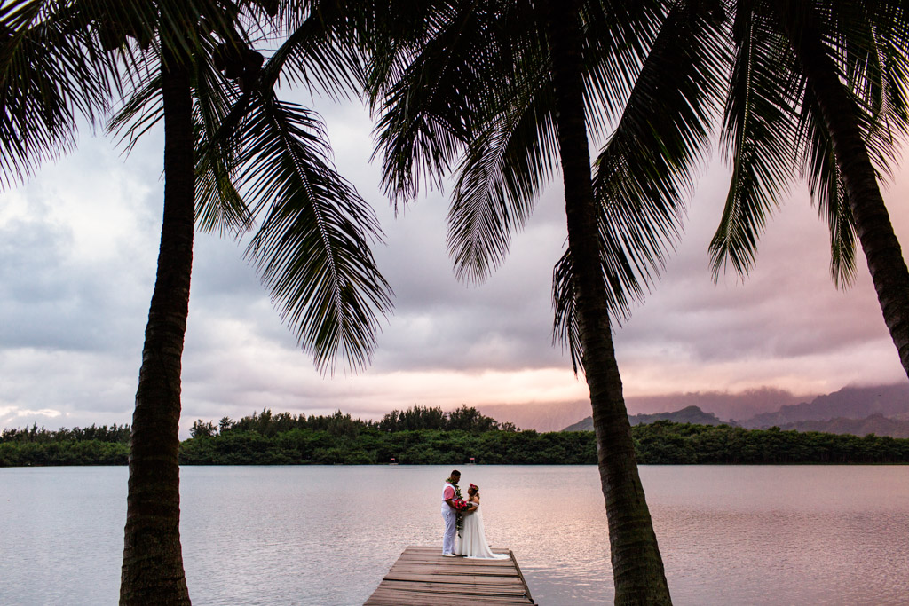 Romantic photo of bride and groom with palm trees at sunset during their Kualoa Ranch wedding in Hawaii
