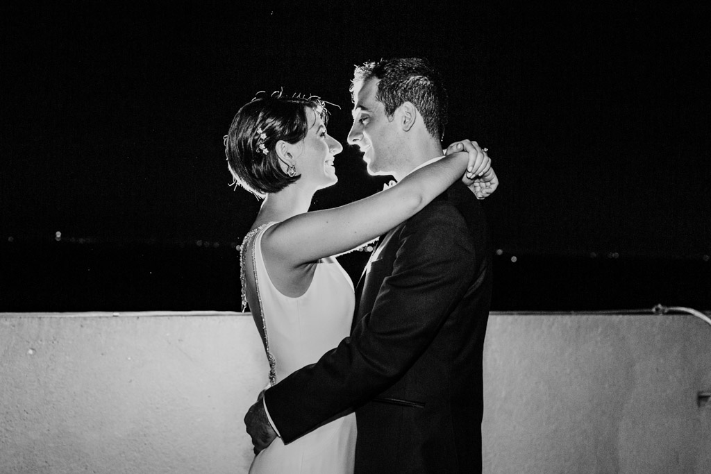 A couple embraces and smiles at each other outdoors at night, dressed in formal attire against the stunning backdrop of Loews Chicago.