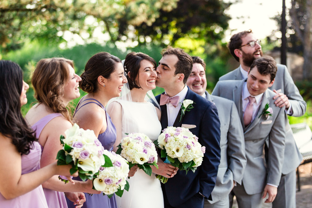 Candid wedding party photo of bride and groom kissing at summer Chicago wedding