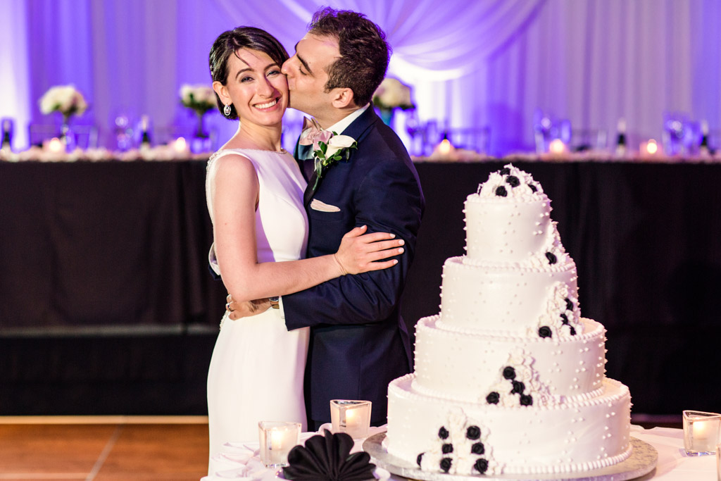 Bride and groom's first kiss with their black and white tiered wedding cake at Loews Chicago hotel