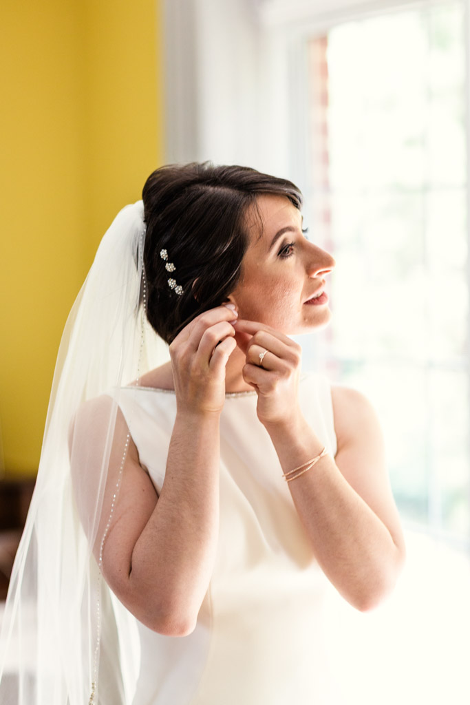 Chicago bride putting on earrings at home before summer Greek Orthodox wedding ceremony