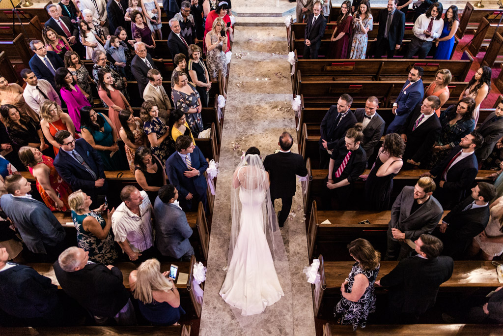 View from balcony of bride and father walking down aisle at Chicago Greek Orthodox wedding ceremony
