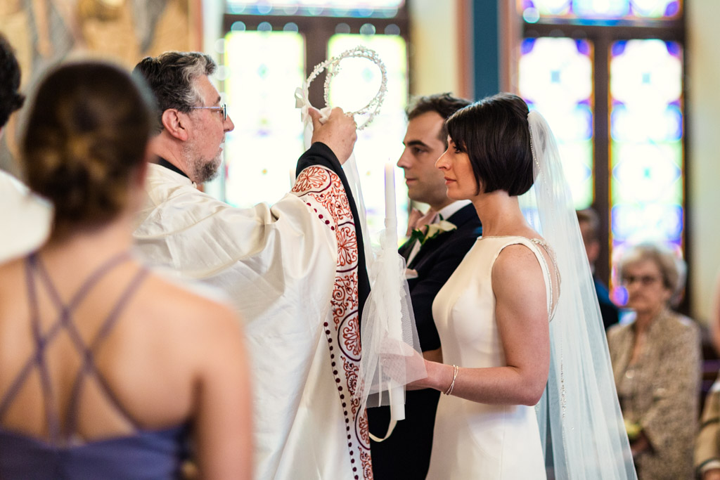 Priest blessing couple with crowns during Chicago Greek Orthodox wedding ceremony at St. George