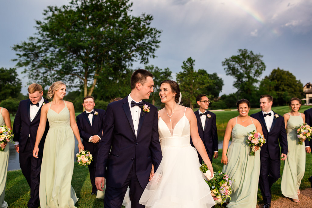 Candid photo of Illinois wedding party walking with bride and groom under rainbow at Sunset Ridge Country Club