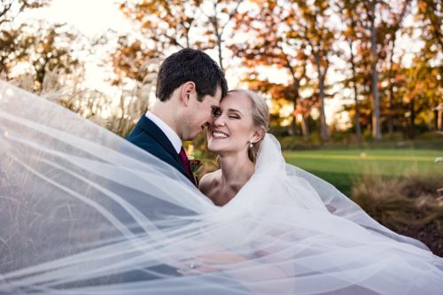 Romantic wedding photo of bride and groom with fall foliage and flowing veil at Crystal Tree Golf Club