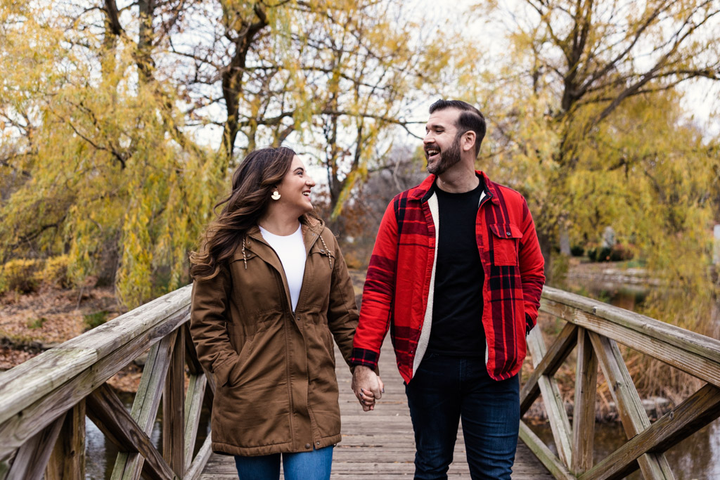 Fall Chicago neighborhood engagement photo of couple walking along bridge with willow trees