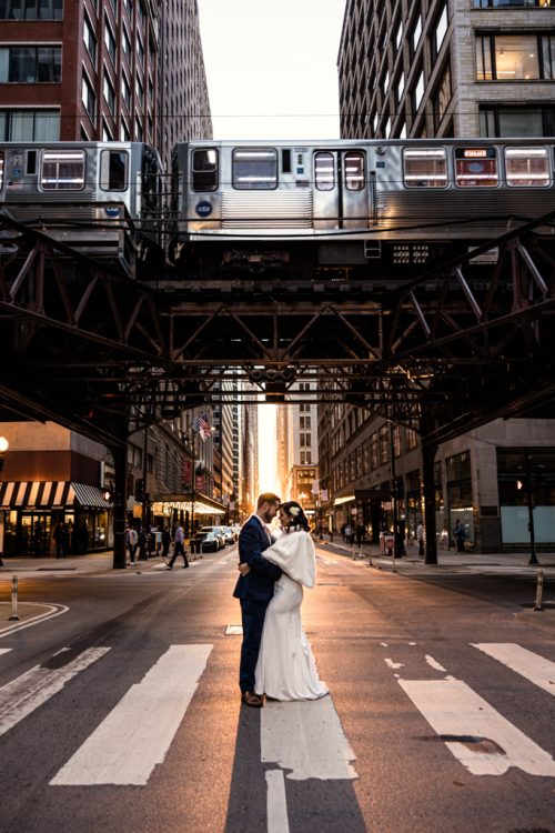 Creative wedding photo of bride and groom standing in street with golden hour light and CTA train going by