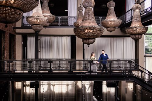 Bride and groom walk along catwalk underneath chandeliers at Artifact Events wedding venue in Chicago