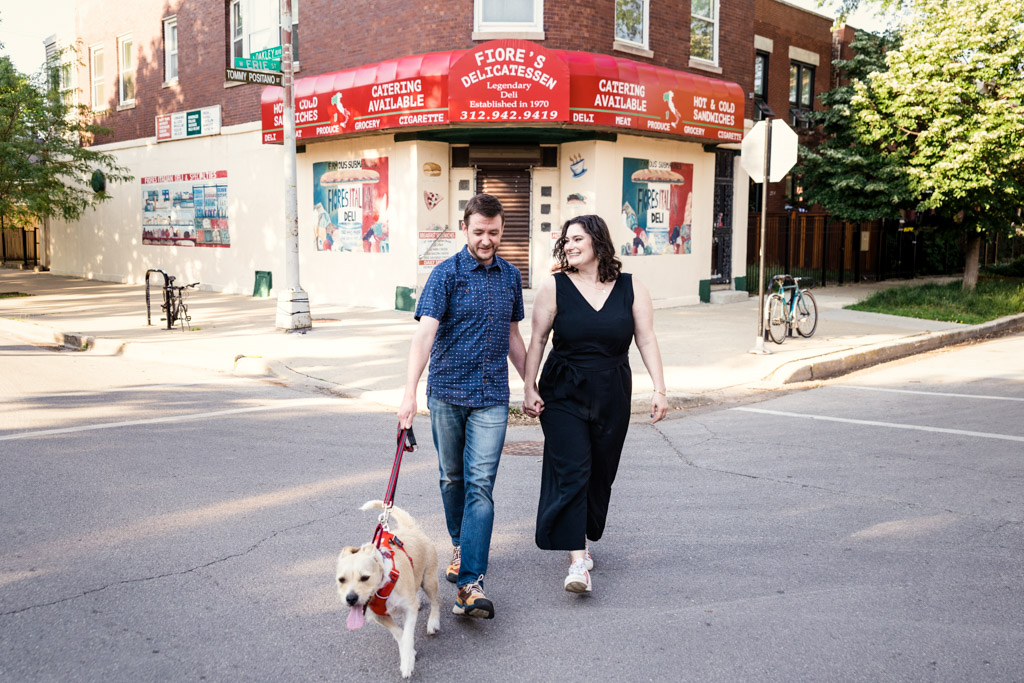 Couple walks their dog in front of local deli during neighborhood engagement session