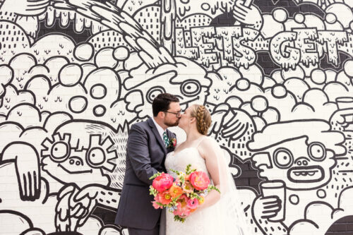 Bride and groom kiss in front of mural outside District Brew Yards in Chicago
