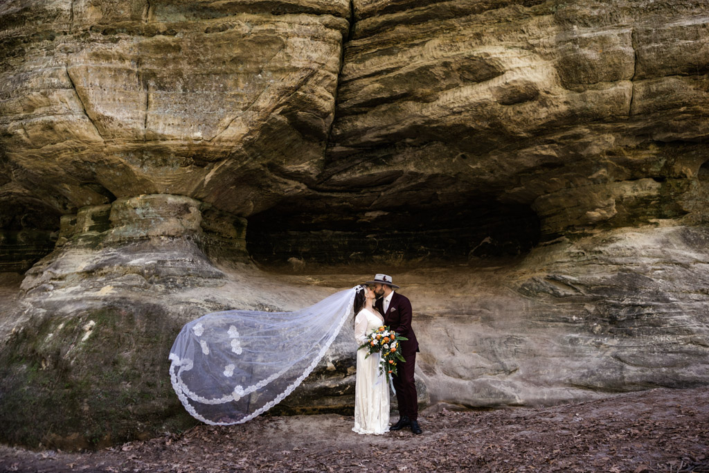 Romantic photo of bride and groom kissing in canyon with vintage veil flowing in the wind at Starved Rock State Park