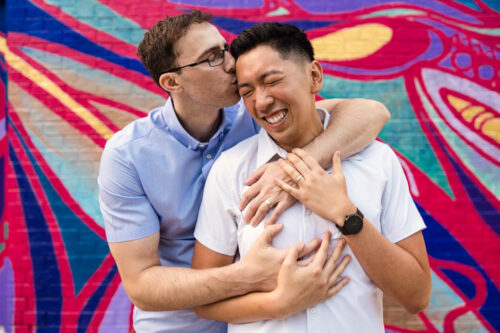 Candid photo of couple embracing with colorful mural during fun summer engagement session