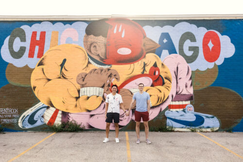 Chicago summer engagement photo of two grooms standing in front of mural in Fulton Market
