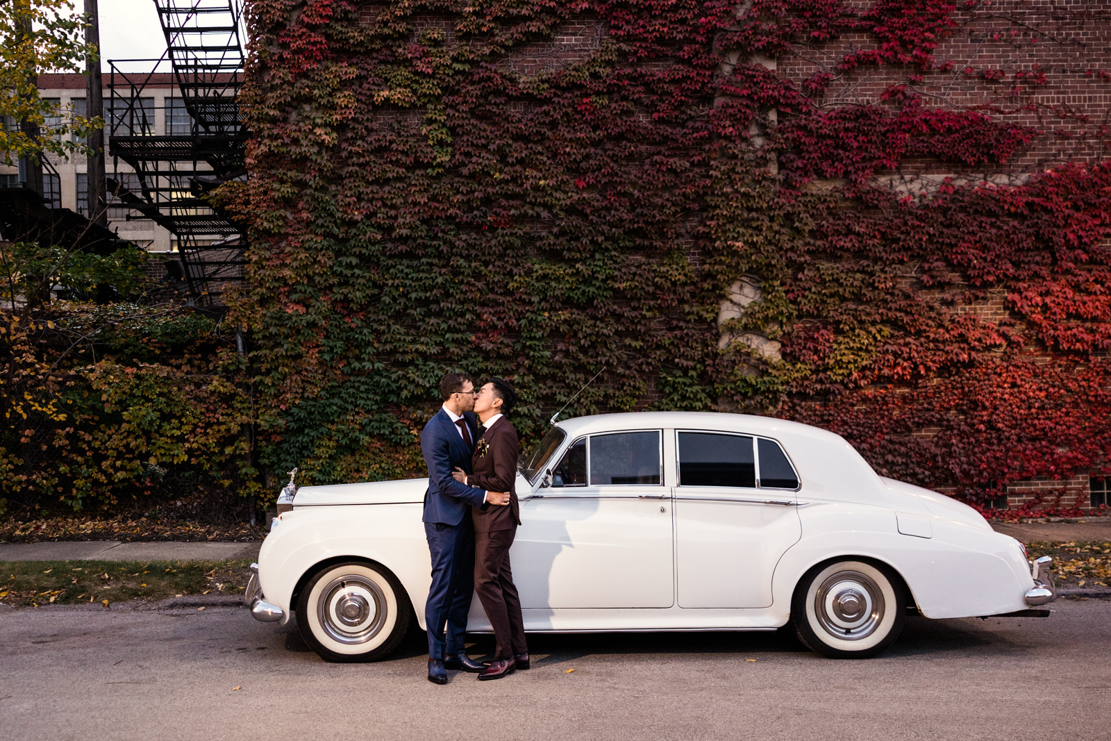 Groom and groom kissing with fall foliage in front of Rolls Royce by Chicago wedding photographer Emma Mullins Photography