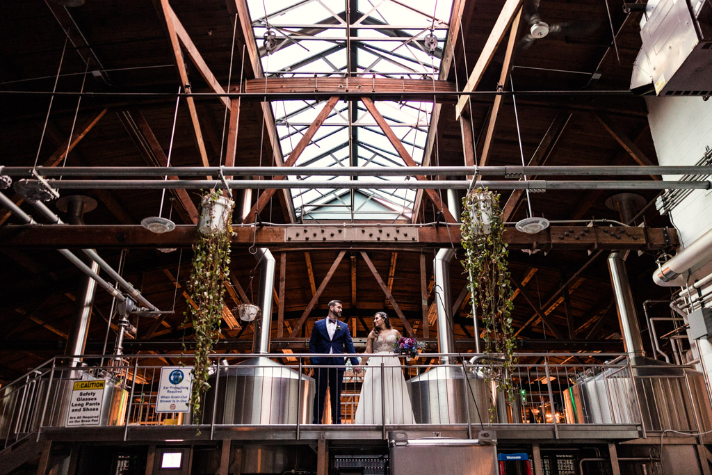 Bride and groom stand under skylight in barrel room at their Chicago Half Acre Brewery wedding