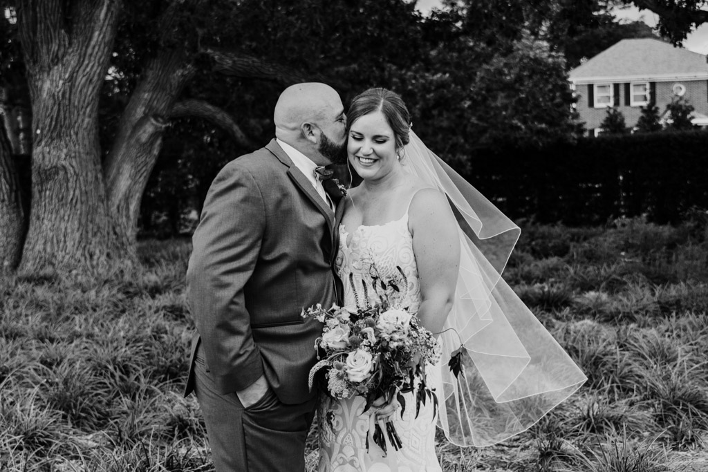 Black and white photo of groom kissing bride on cheek at their summer Cantigny wedding