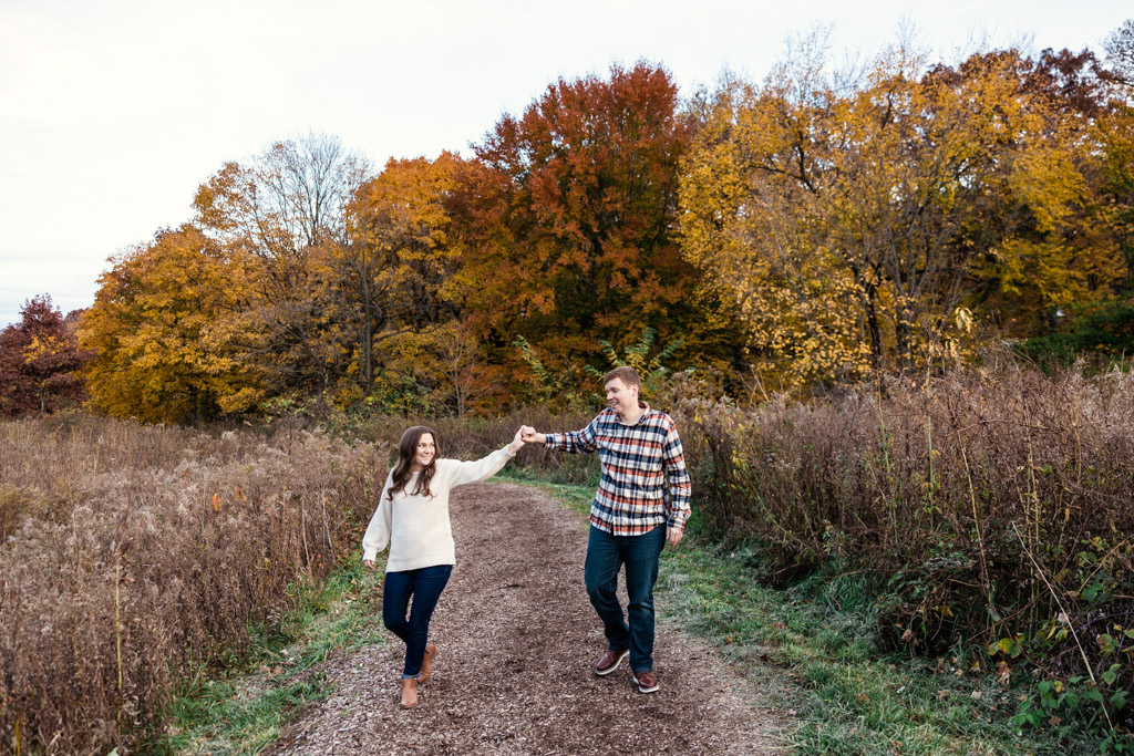 Engaged couple holds hands in front of fall foliage during their Morton Arboretum engagement session