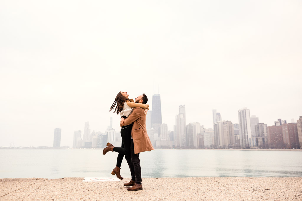 Fun winter engagement photo of couple with Chicago skyline at North Avenue Beach lakefront