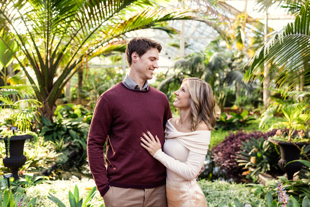 Candid Garfield Park Conservatory engagement photo of couple smiling in Palm House with tropical plants