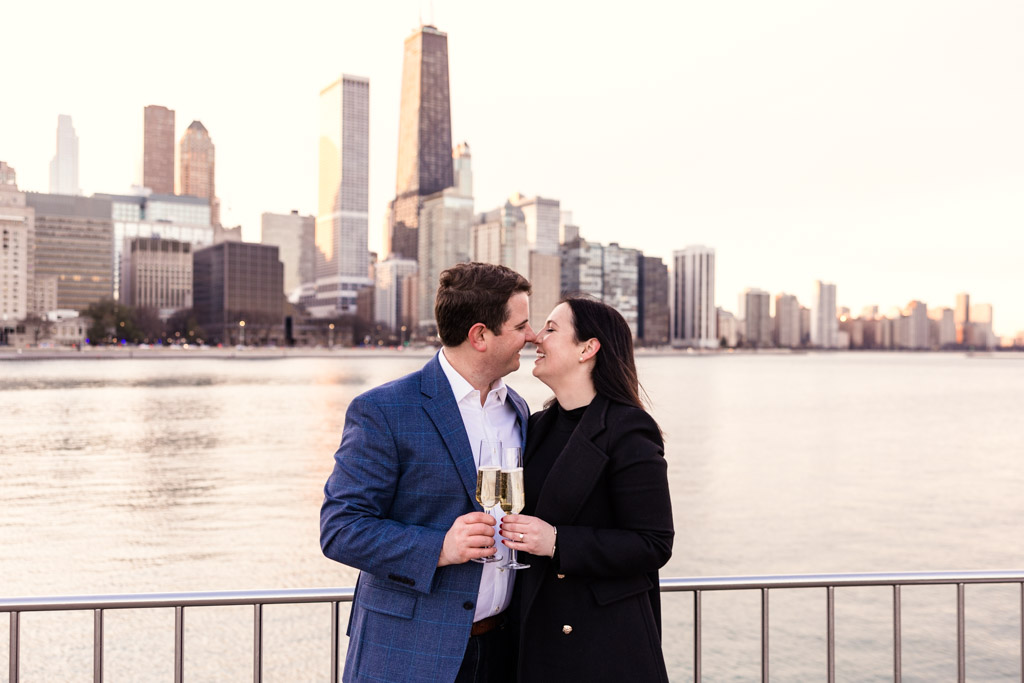 Couple kiss in front of skyline view at Olive Park with champagne during their Chicago winter engagement session