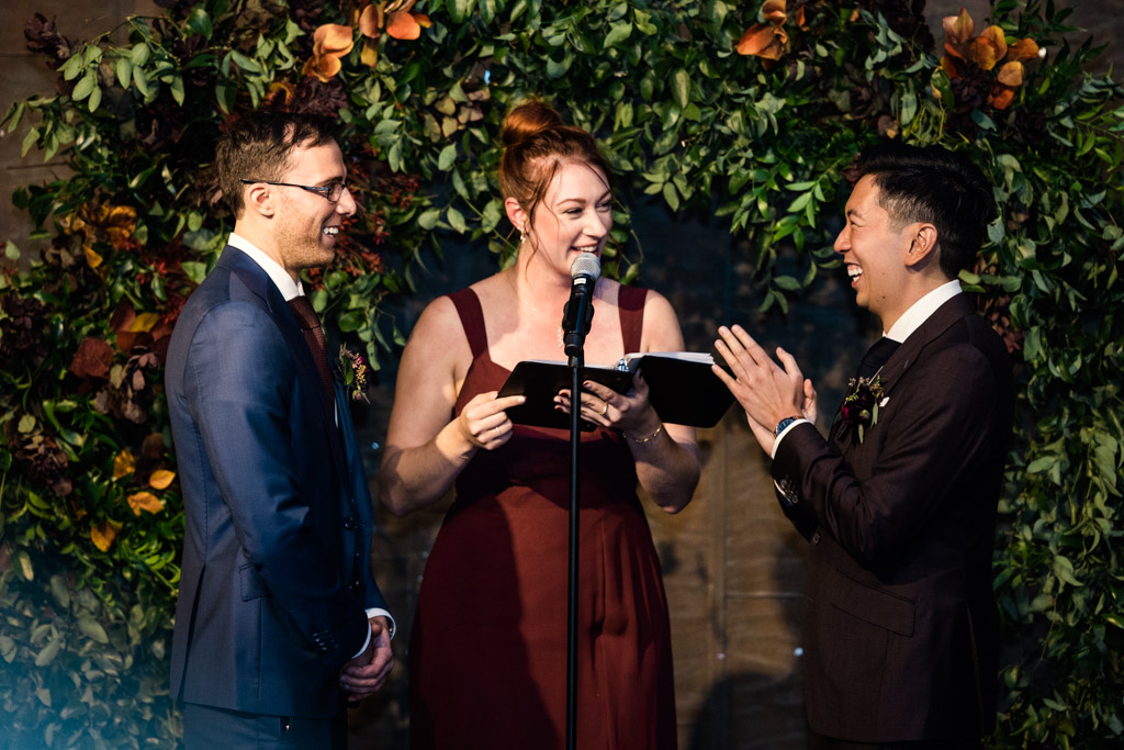 Candid photo of groom and groom during wedding ceremony at Ovation Chicago surrounded by greenery and floral arch