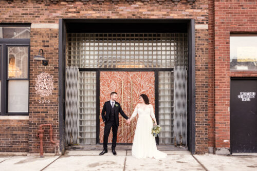 Bride and groom stand in front of mural on door at The Arbory before their Chicago winter wedding ceremony