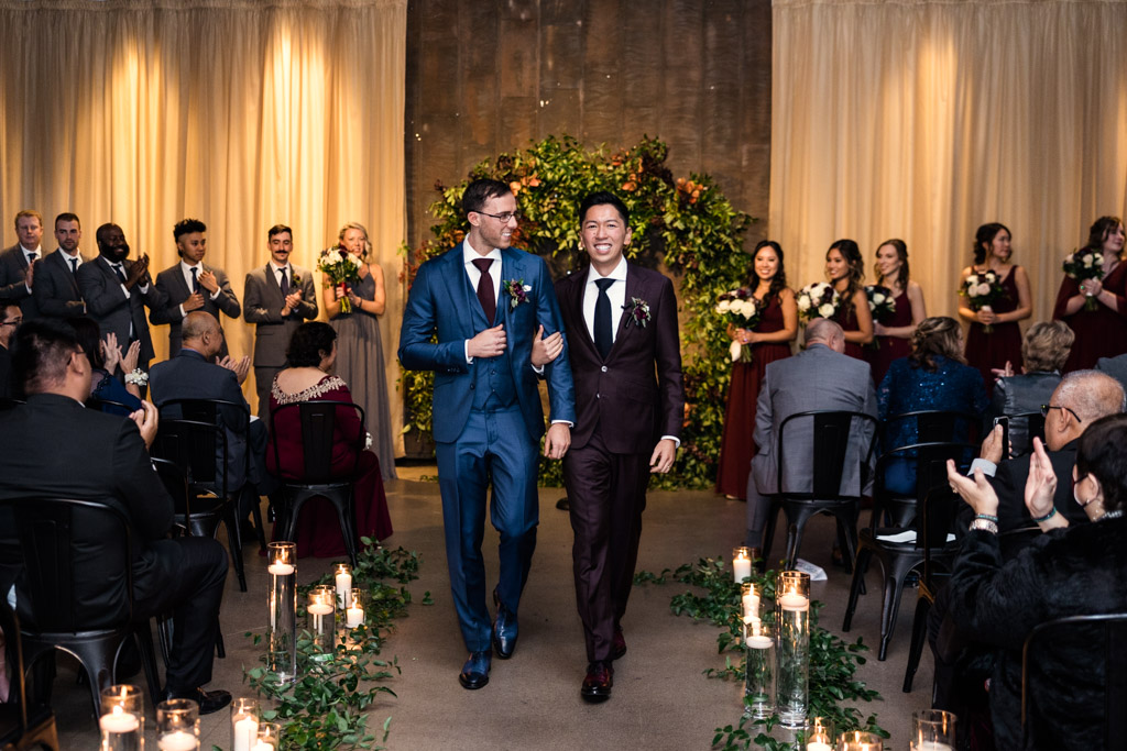 Two happy grooms exit their fall wedding ceremony at Ovation Chicago as guests applaud