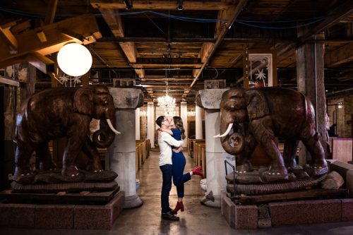 Unique photo of couple kissing between antique elephant statues during their Salvage One engagement session