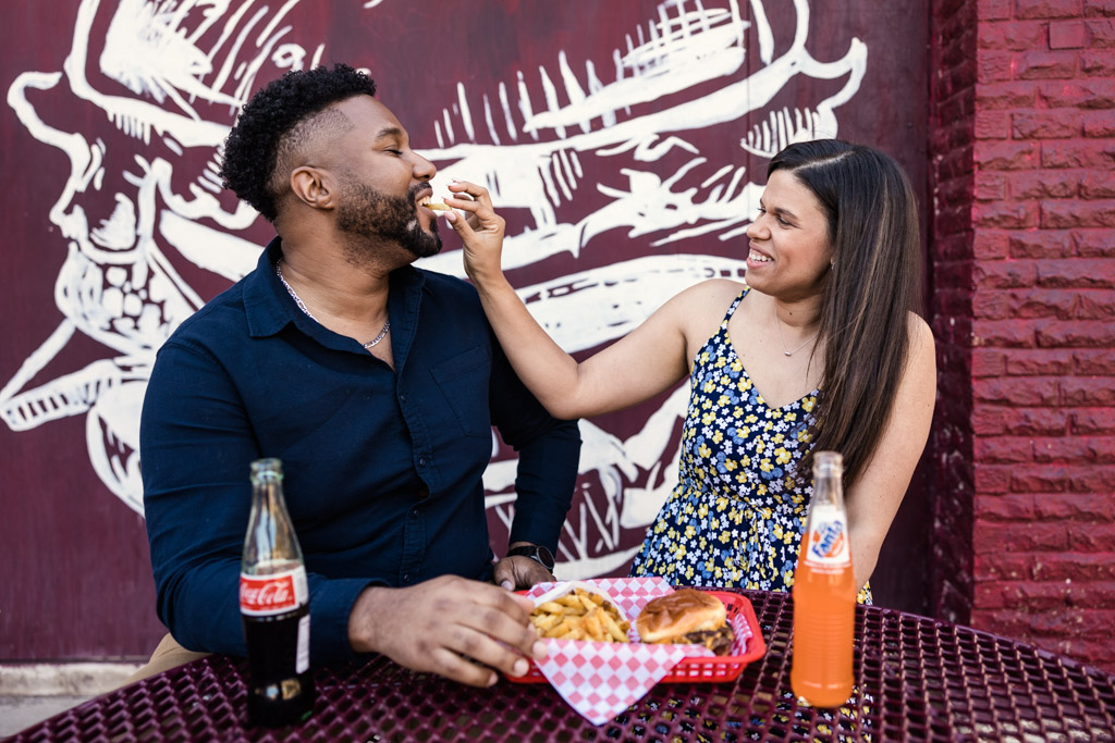 Fun photo of couple feeding each other French fries at Small Cheval during summer Wicker Park engagement session