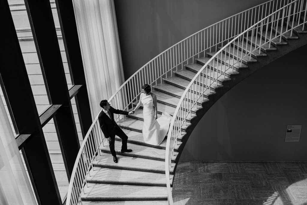 Black and white photo of bride and groom walking down iconic spiral staircase at Art Institute of Chicago