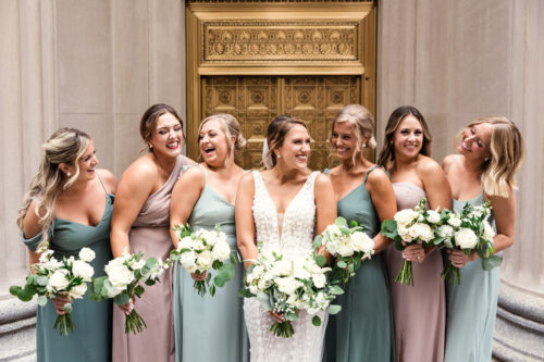 Candid photo of bridesmaids and bride laughing in front of gold doors downtown Chicago
