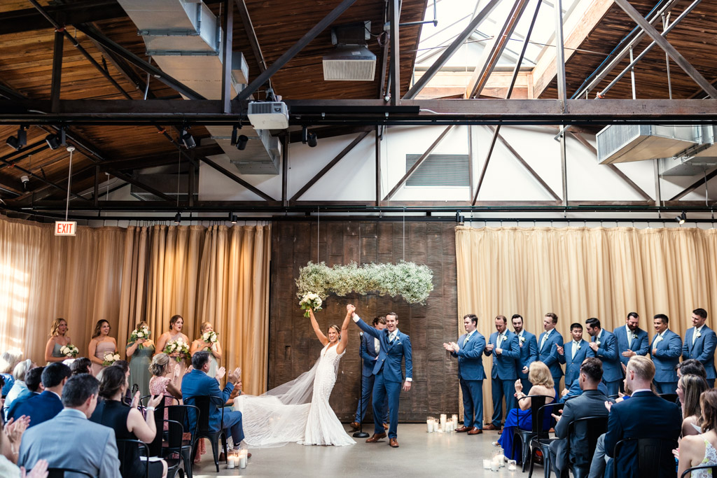 Just married bride and groom cheer with their guests under skylight at Ovation Chicago wedding ceremony