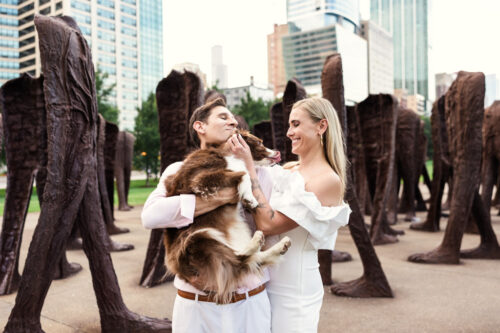 Candid engagement photo of couple laughing with dog and Agora sculptures in South Loop