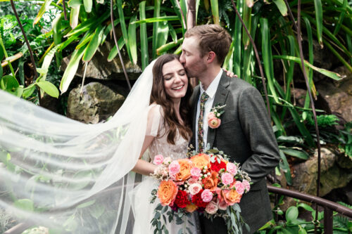 Romantic photo of bride and groom surrounded by greenery at Garfield Park Conservatory with flowing veil and vibrant florals