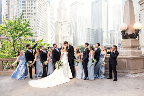 Bride and groom kiss outside Wrigley Building while wedding party cheers before downtown Chicago wedding at Pazzo's 311