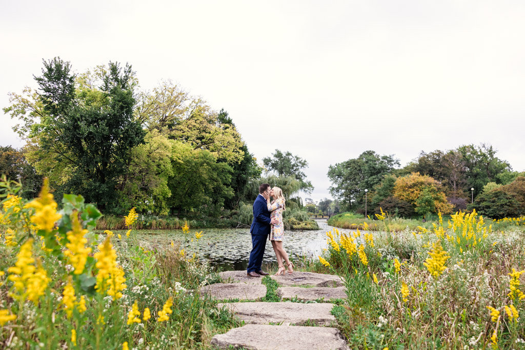 Romantic photo of couple kissing at Humboldt Park lagoon with yellow wildflowers during September engagement session in Chicago