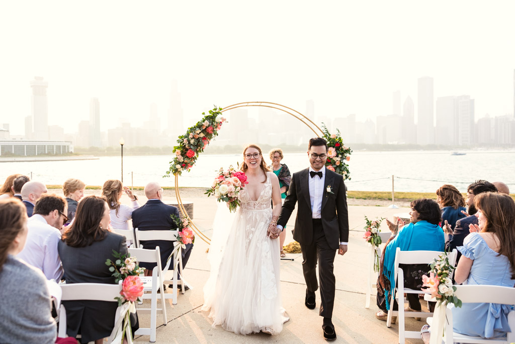 Just married bride and groom exit their outdoor wedding ceremony at Adler Planetarium with Chicago skyline view