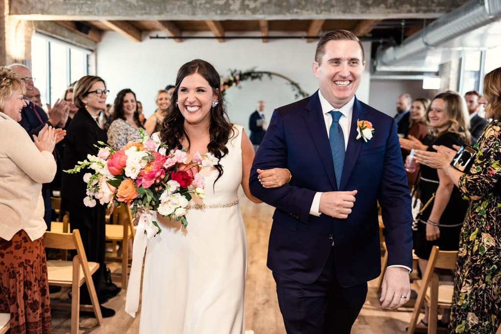 Happy bride and groom exit their spring Walden wedding ceremony as guests cheer
