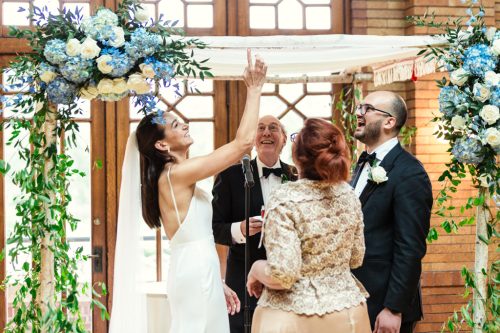 Bride touches honey to Chuppah during Albanian and Jewish wedding ceremony at Cafe Brauer Great Hall