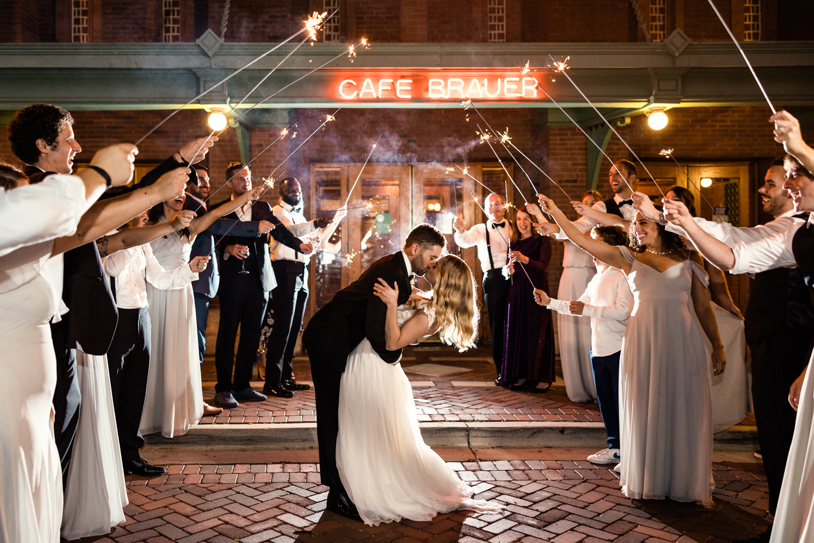 Bride and groom kiss in front of Cafe Brauer at night during romantic sparkler exit by Chicago wedding photographer Emma Mullins Photography
