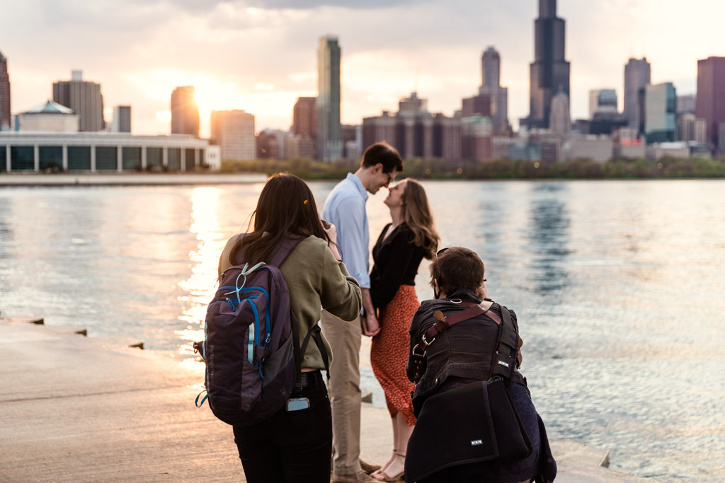 Romantic photo of two photographers with engaged couple in front of Chicago skyline during live shoot photography mentor session with Emma Mullins Photography