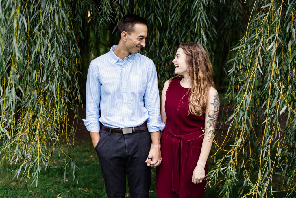 Candid photo of happy couple smiling under willow tree during their Winnemac Park engagement session