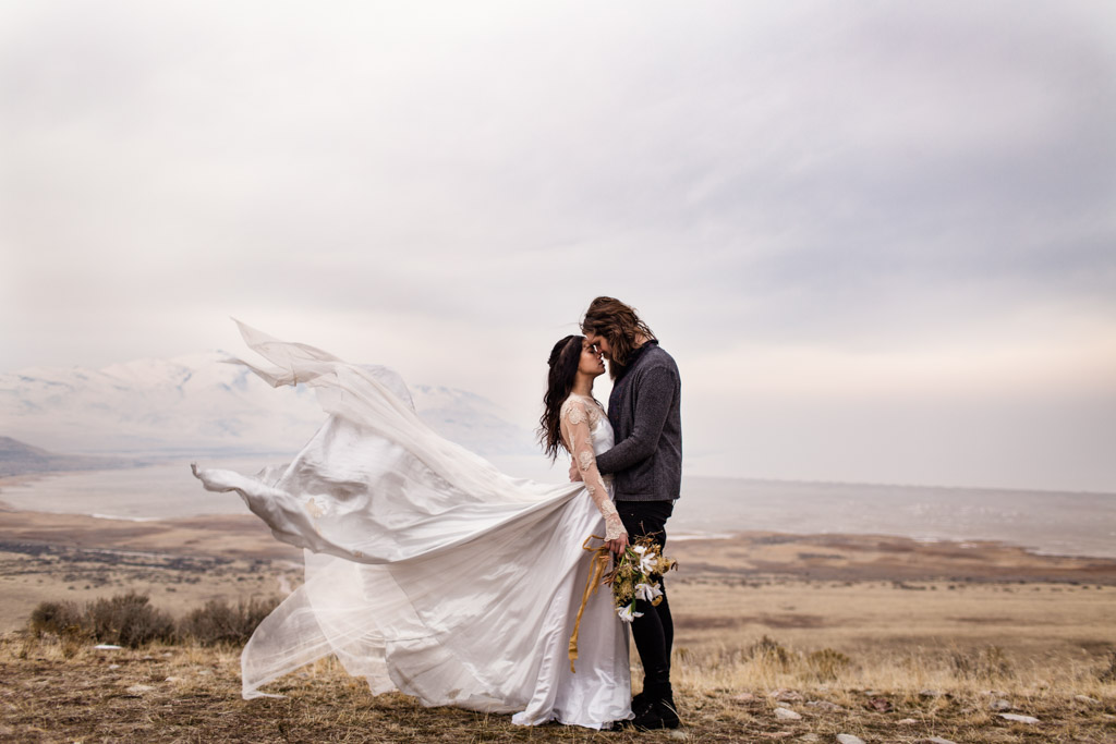 Romantic Antelope Island elopement photo of bride and groom on mountain with dress flowing in the wind