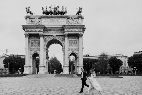 Fun photo of bride and groom running in front of Arco della Pace in Sempione Park after their Milan, Italy destination wedding